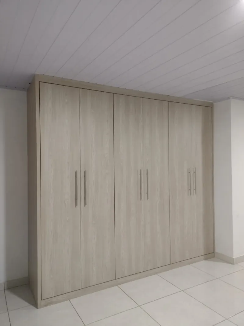 Guarda-roupa de seis portas em MDF amadeirado claro instalado do piso ao teto no quarto