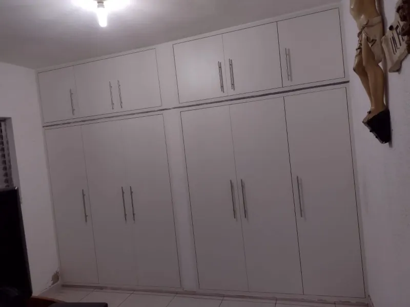 Guarda-roupa embutido branco ocupando a parede inteira do quarto, com maleiros na parte superior